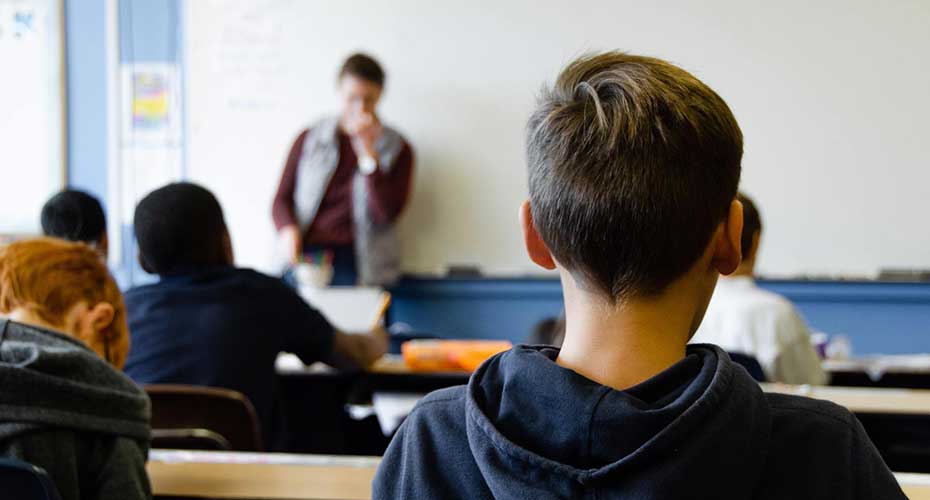 Teacher at front of classroom with back of boy.